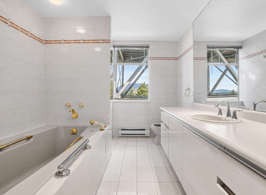 This spacious bathroom features a luxurious bathtub with gold-toned fixtures and a sleek vanity with a double sink.
