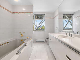 This spacious bathroom features a luxurious bathtub with gold-toned fixtures and a sleek vanity with a double sink.
