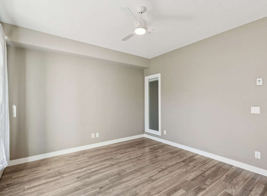 Experience modern living in this spacious room featuring a sleek ceiling fan and elegant wood-look flooring.