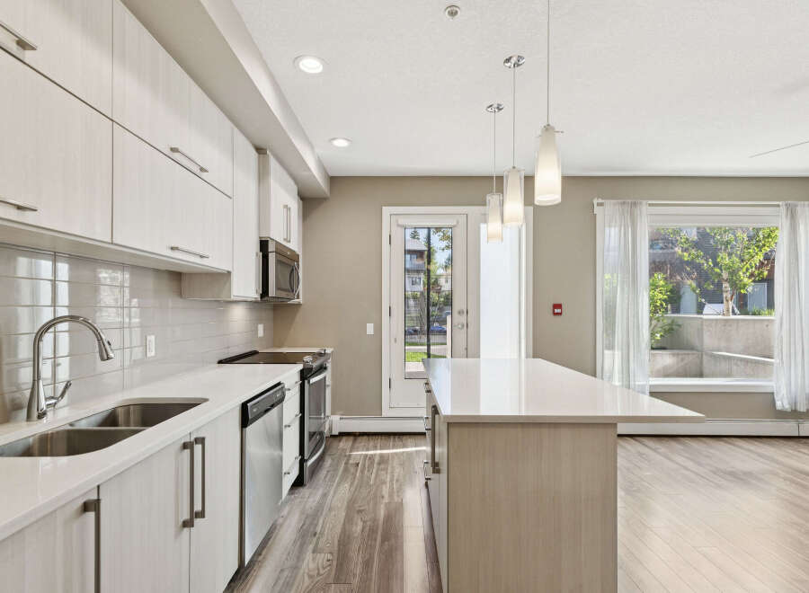 Experience modern living in this stunning kitchen featuring sleek white cabinetry, a spacious quartz island, and a complementary tiled backsplash.