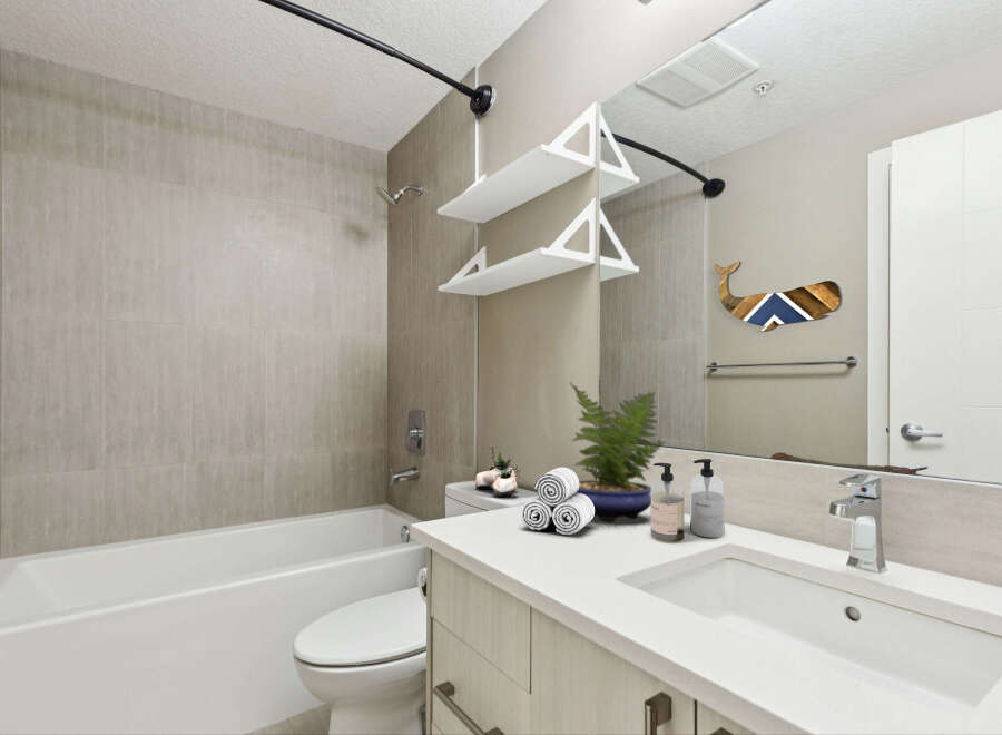 This modern bathroom features a sleek bathtub and toilet, complemented by a stylish vanity with a white countertop and integrated sink.