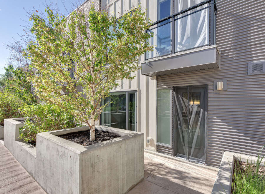 Experience modern urban living with this stunning property featuring sleek corrugated metal siding and a private balcony overlooking lush greenery.