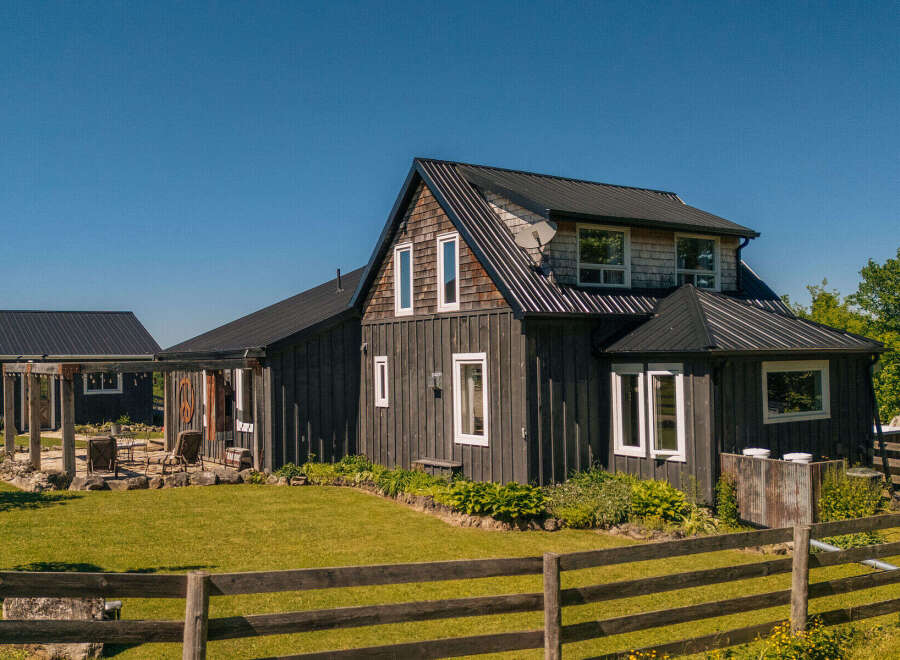 Experience rustic charm and modern comfort in this beautifully renovated farmhouse, featuring dark wood siding and a sleek metal roof.