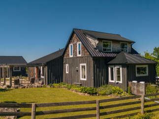 Experience rustic charm and modern comfort in this beautifully renovated farmhouse, featuring dark wood siding and a sleek metal roof.