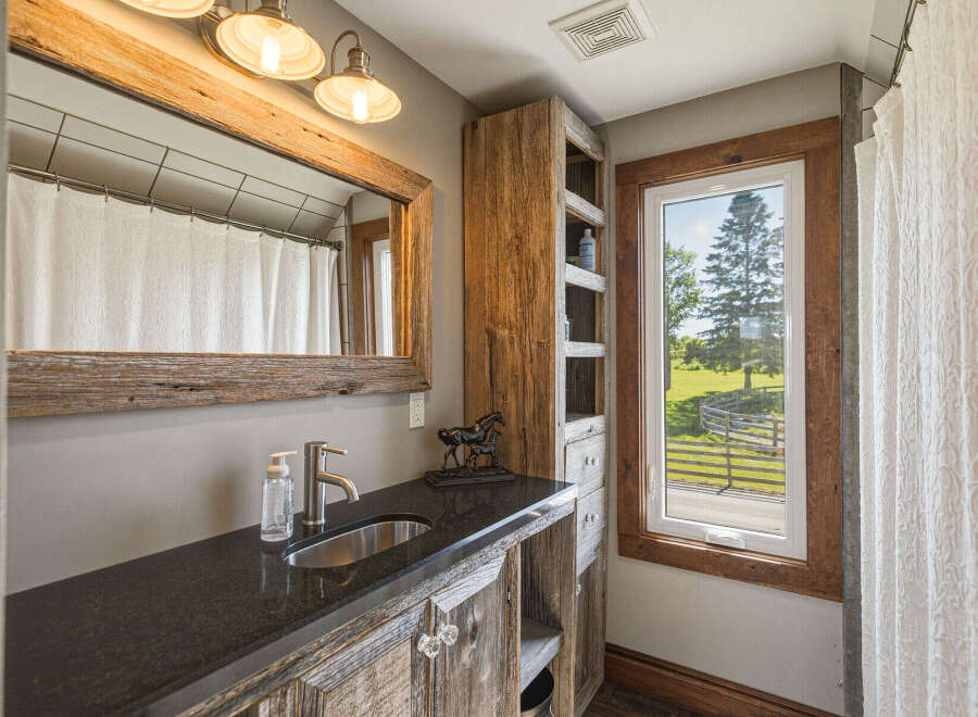 This rustic bathroom features a charming vanity with a granite countertop and a stainless steel sink, complemented by weathered wood cabinetry and a large, reclaimed wood mirror.