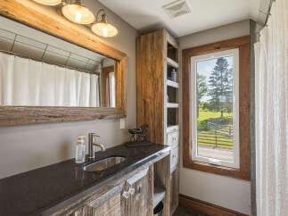 This rustic bathroom features a charming vanity with a granite countertop and a stainless steel sink, complemented by weathered wood cabinetry and a large, reclaimed wood mirror.
