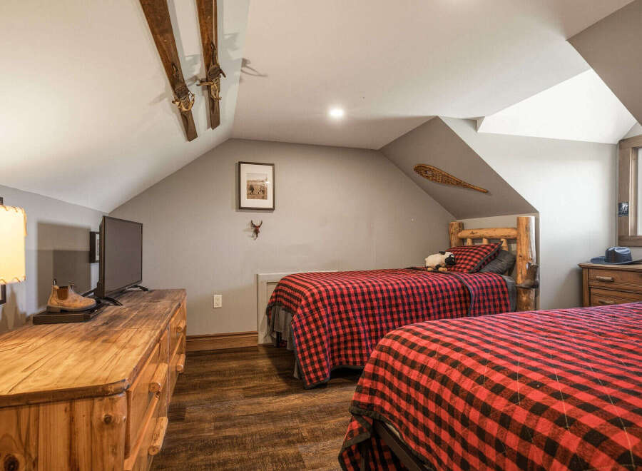 This charming attic bedroom features two cozy beds with rustic red and black buffalo plaid bedding, perfect for a mountain retreat.
