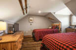 This charming attic bedroom features two cozy beds with rustic red and black buffalo plaid bedding, perfect for a mountain retreat.