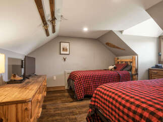 This charming attic bedroom features two cozy beds with rustic red and black buffalo plaid bedding, perfect for a mountain retreat.