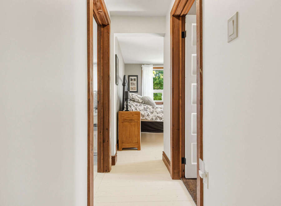 Step into a charming bedroom through a rustic wooden doorway, offering a glimpse of a cozy bed adorned with a floral duvet and a quaint nightstand.