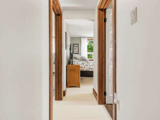 Step into a charming bedroom through a rustic wooden doorway, offering a glimpse of a cozy bed adorned with a floral duvet and a quaint nightstand.