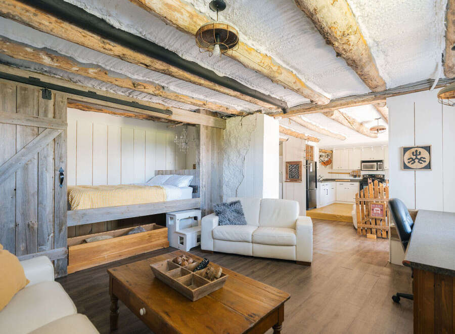 Experience rustic charm in this unique living space featuring exposed log beams and a cozy lofted bed accessible by a sliding barn door.