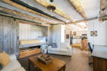 Experience rustic charm in this unique living space featuring exposed log beams and a cozy lofted bed accessible by a sliding barn door.
