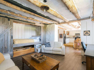 Experience rustic charm in this unique living space featuring exposed log beams and a cozy lofted bed accessible by a sliding barn door.