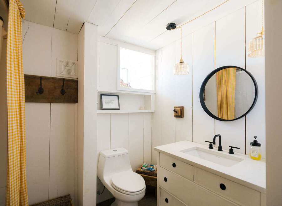 This charming bathroom features a white shiplap design, a rustic wooden coat rack, and a bright yellow gingham shower curtain.