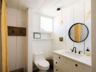 This charming bathroom features a white shiplap design, a rustic wooden coat rack, and a bright yellow gingham shower curtain.