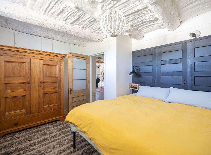 Experience rustic charm in this unique bedroom featuring a striking dark wood paneled headboard and a vibrant yellow duvet.