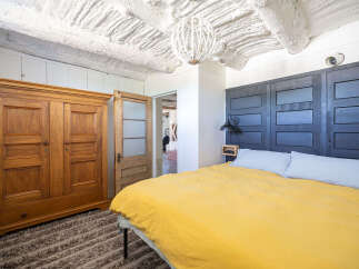 Experience rustic charm in this unique bedroom featuring a striking dark wood paneled headboard and a vibrant yellow duvet.