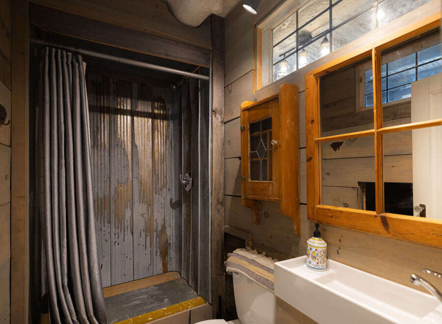 This rustic bathroom features a unique corrugated metal shower with a grey textured curtain, adding a touch of industrial charm.