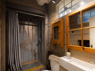 This rustic bathroom features a unique corrugated metal shower with a grey textured curtain, adding a touch of industrial charm.