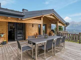 Experience breathtaking mountain views from this stunning wooden chalet, featuring a spacious outdoor dining area perfect for al fresco meals.