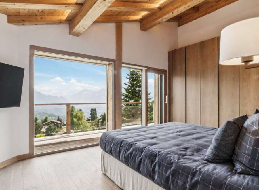 Experience breathtaking mountain views from this luxurious bedroom, featuring a spacious king-sized bed with a stylish grey plaid comforter and matching pillows.