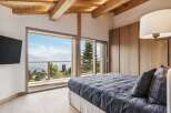Experience breathtaking mountain views from this luxurious bedroom, featuring a spacious king-sized bed with a stylish grey plaid comforter and matching pillows.