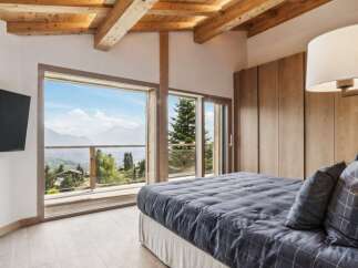 Experience breathtaking mountain views from this luxurious bedroom, featuring a spacious king-sized bed with a stylish grey plaid comforter and matching pillows.