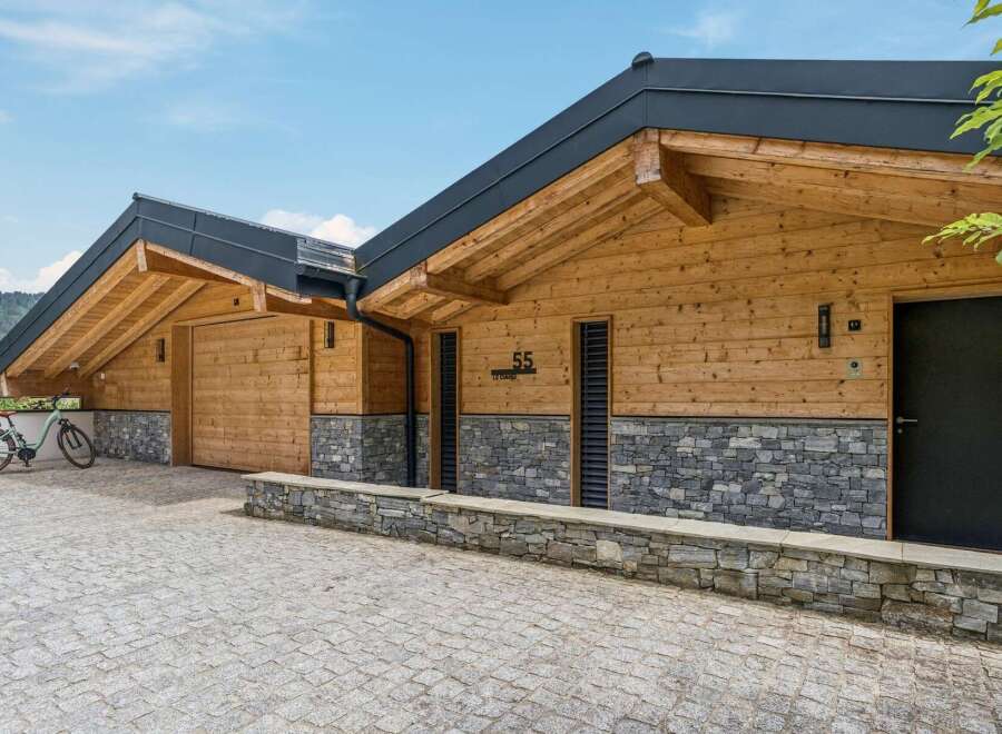 Experience modern alpine living in this stunning wooden chalet, featuring a striking stone base and exposed timber beams under a sleek dark roof.