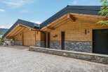 Experience modern alpine living in this stunning wooden chalet, featuring a striking stone base and exposed timber beams under a sleek dark roof.