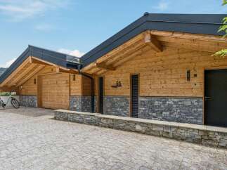Experience modern alpine living in this stunning wooden chalet, featuring a striking stone base and exposed timber beams under a sleek dark roof.