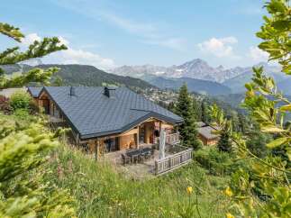 Experience breathtaking mountain views from this stunning wooden chalet, perfectly nestled amidst lush greenery.
