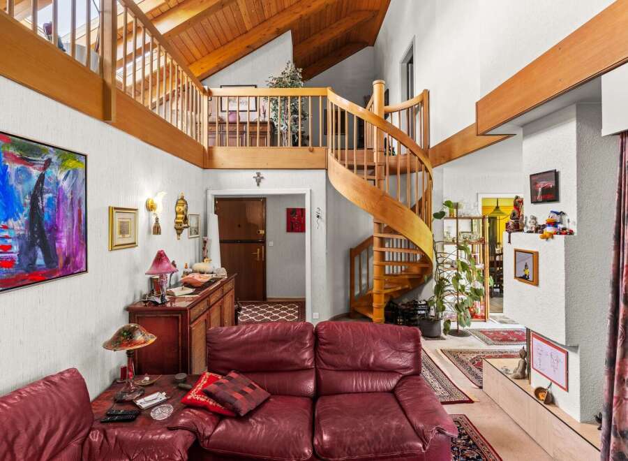 This spacious living area boasts a stunning wooden spiral staircase leading to a lofted area with exposed beams and a vaulted ceiling.