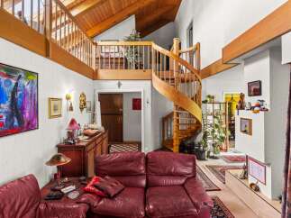 This spacious living area boasts a stunning wooden spiral staircase leading to a lofted area with exposed beams and a vaulted ceiling.