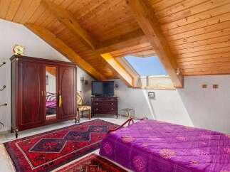 Discover this charming attic bedroom featuring a spacious wooden wardrobe and a vibrant purple quilted bedspread.
