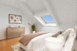 Experience modern living in this charming attic bedroom, featuring a unique sloped ceiling with exposed beams and a large skylight that floods the space with natural light.
