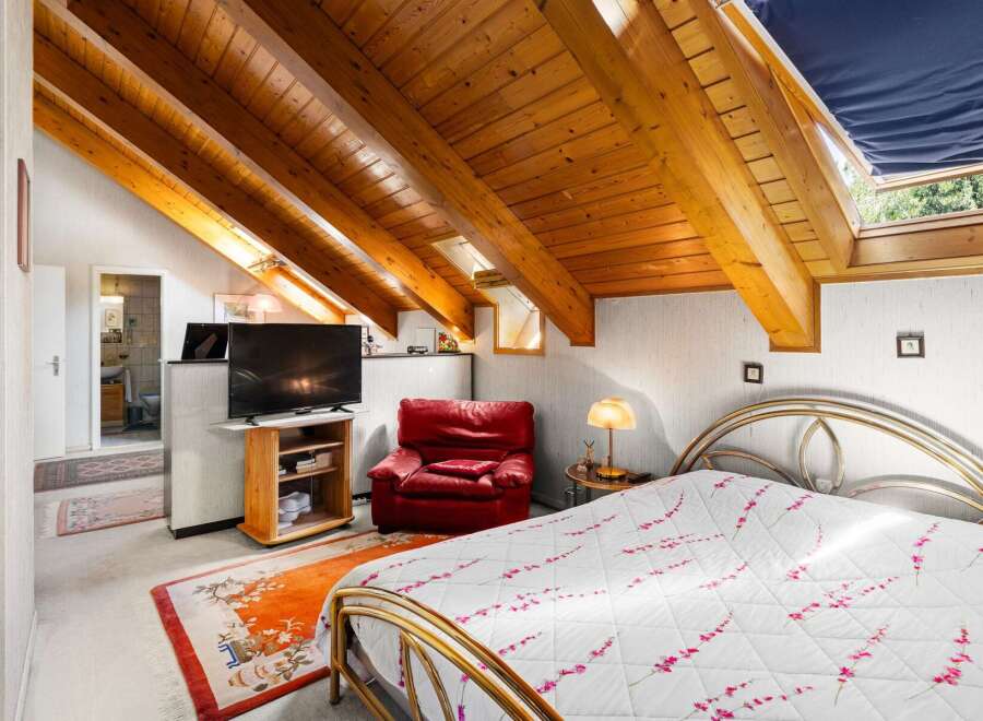 Discover this charming attic bedroom featuring a cozy red armchair and a modern television setup.