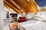 Discover this charming attic bedroom featuring a cozy red armchair and a modern television setup.
