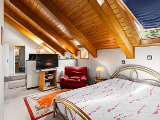 Discover this charming attic bedroom featuring a cozy red armchair and a modern television setup.
