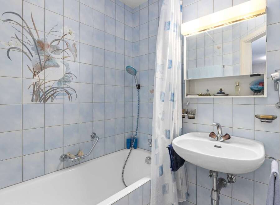 This charming bathroom features a bathtub with a showerhead and a decorative tile mural of a bird and flowers.
