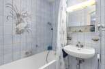 This charming bathroom features a bathtub with a showerhead and a decorative tile mural of a bird and flowers.