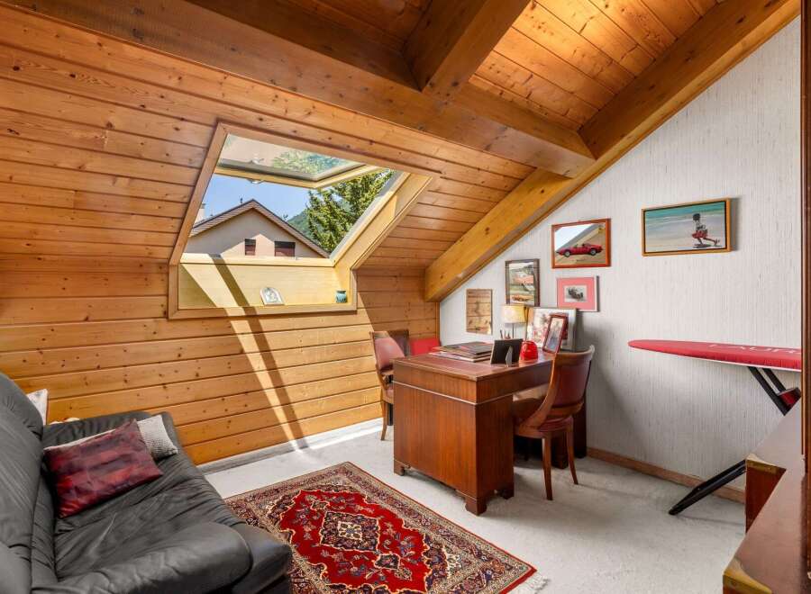 Discover this charming attic room, featuring a cozy black leather sofa and a traditional red oriental rug.