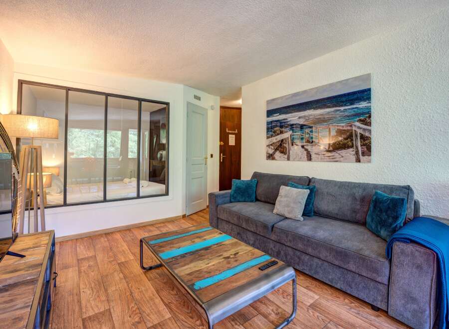 Experience coastal charm in this inviting living space, featuring a comfortable grey sofa adorned with plush teal and grey cushions, perfect for relaxing after a day at the beach.