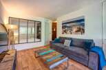 Experience coastal charm in this inviting living space, featuring a comfortable grey sofa adorned with plush teal and grey cushions, perfect for relaxing after a day at the beach.