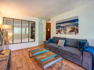 Experience coastal charm in this inviting living space, featuring a comfortable grey sofa adorned with plush teal and grey cushions, perfect for relaxing after a day at the beach.