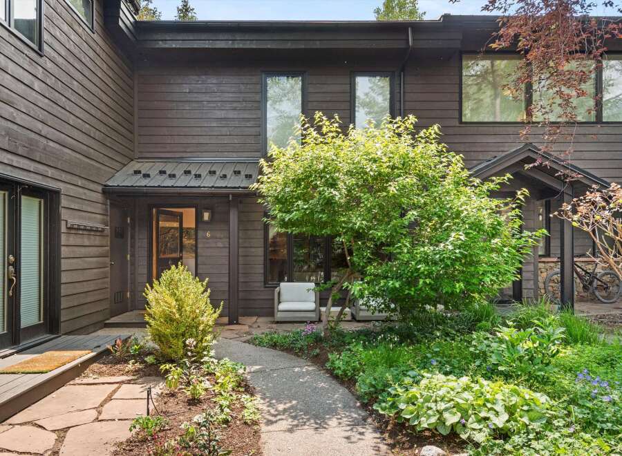 Discover this charming home featuring a welcoming entryway with a stone pathway leading through lush landscaping.