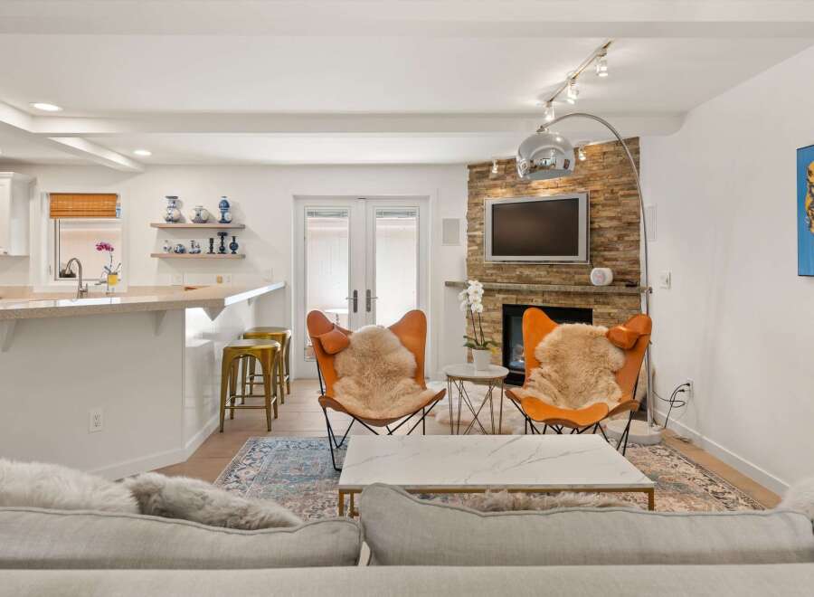 Experience modern living in this stylish open-concept space, featuring a sleek kitchen island with bar seating and a cozy living area centered around a stone-clad fireplace.