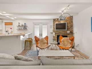 Experience modern living in this stylish open-concept space, featuring a sleek kitchen island with bar seating and a cozy living area centered around a stone-clad fireplace.