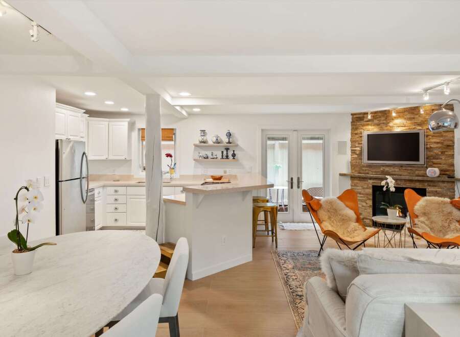 Experience modern living in this open-concept space featuring a sleek kitchen with white cabinetry and stainless steel appliances, flowing seamlessly into a cozy living area.
