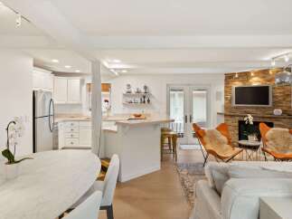 Experience modern living in this open-concept space featuring a sleek kitchen with white cabinetry and stainless steel appliances, flowing seamlessly into a cozy living area.
